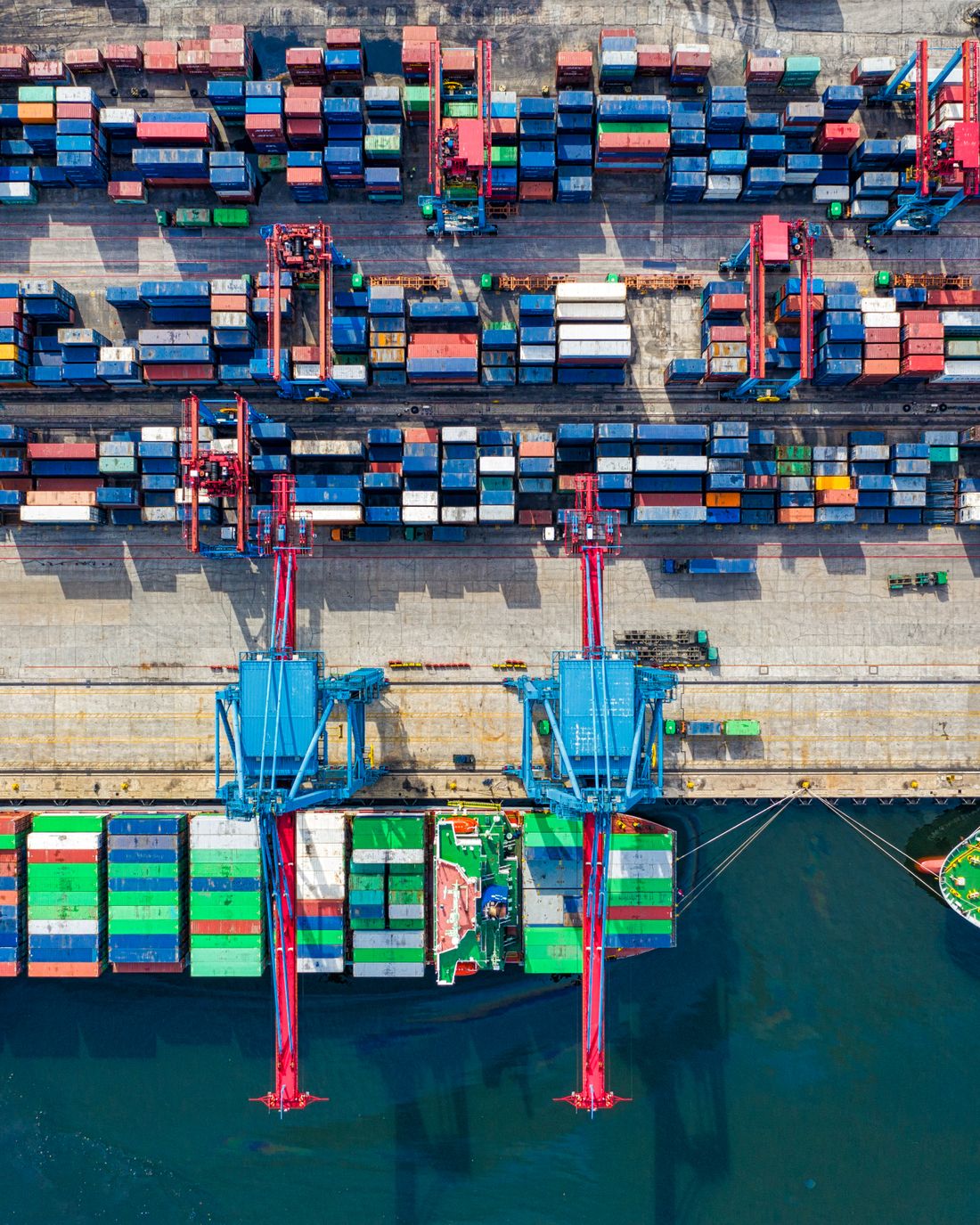 Vue aérienne d'un terminal à conteneurs : portiques de quai chargeant des conteneurs sur un porte-conteneurs.